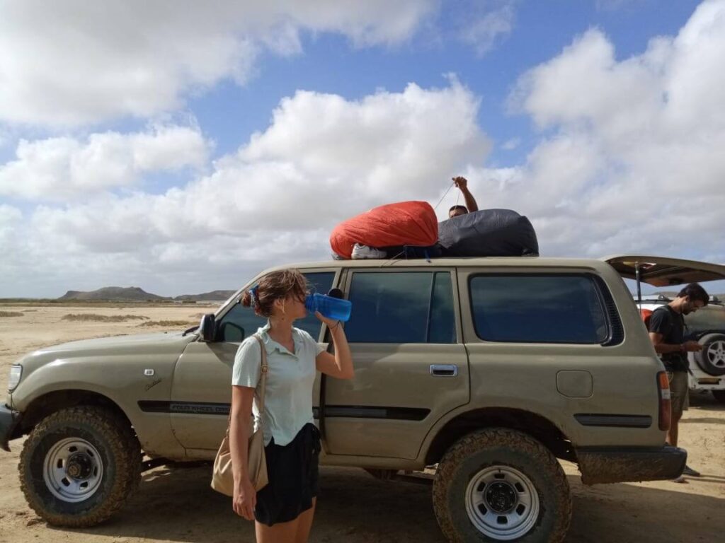 Ik sta hier voor een jeep uit m'n waterfles te drinken. Op de jeep liggen onze backpacks vastgebonden