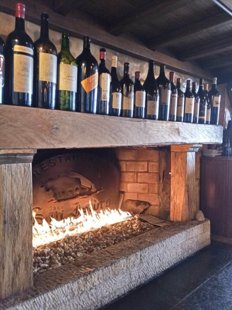 een open haard met vuur erin en allemaal lege flessen wijn bovenop de haard