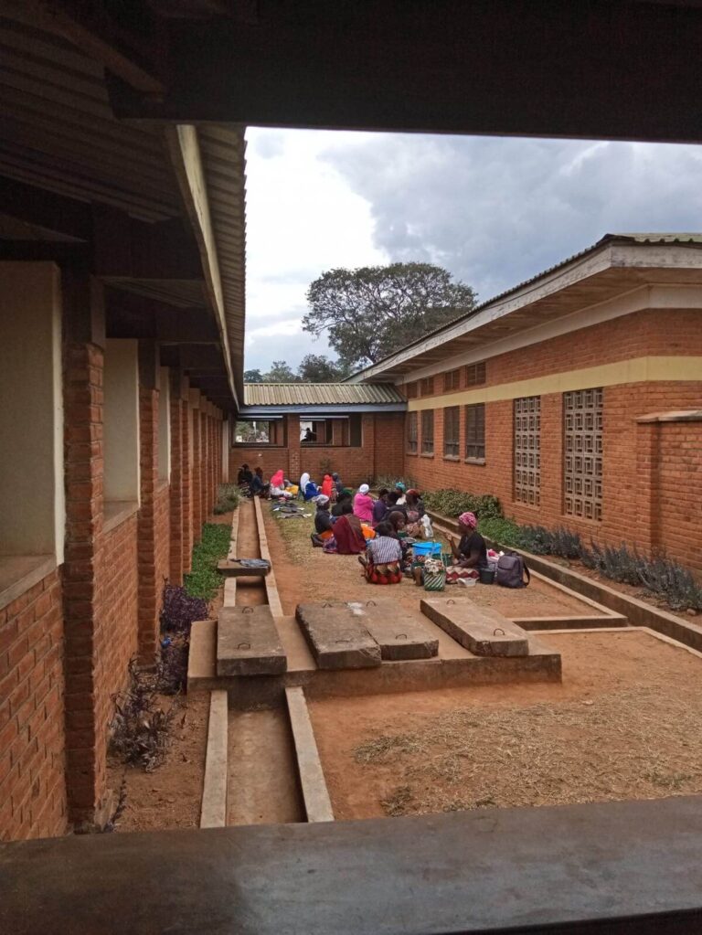Tussen 2 muren van het ziekenhuis zitten lokale families op kleedjes op de grond