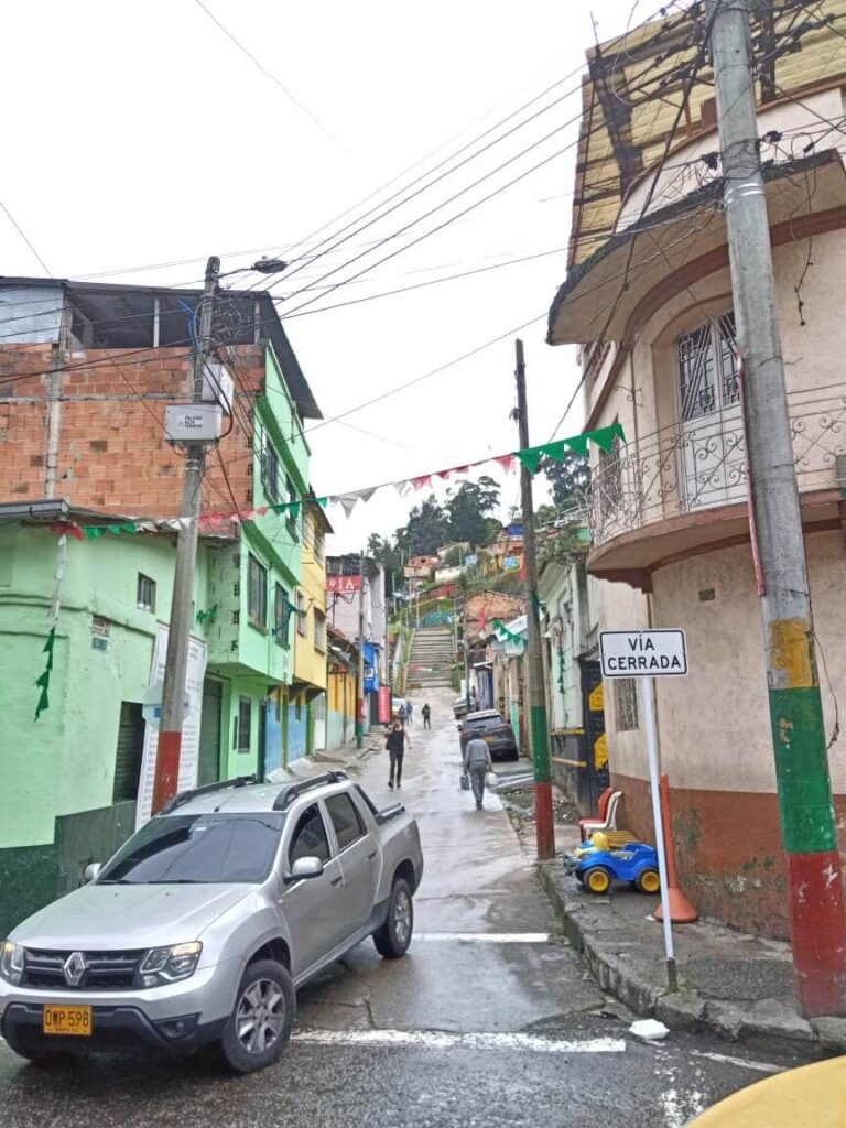een straat in Bogotá met verschillende huizen waarvan er 1 lichtgroen is. Er rijdt een auto voor