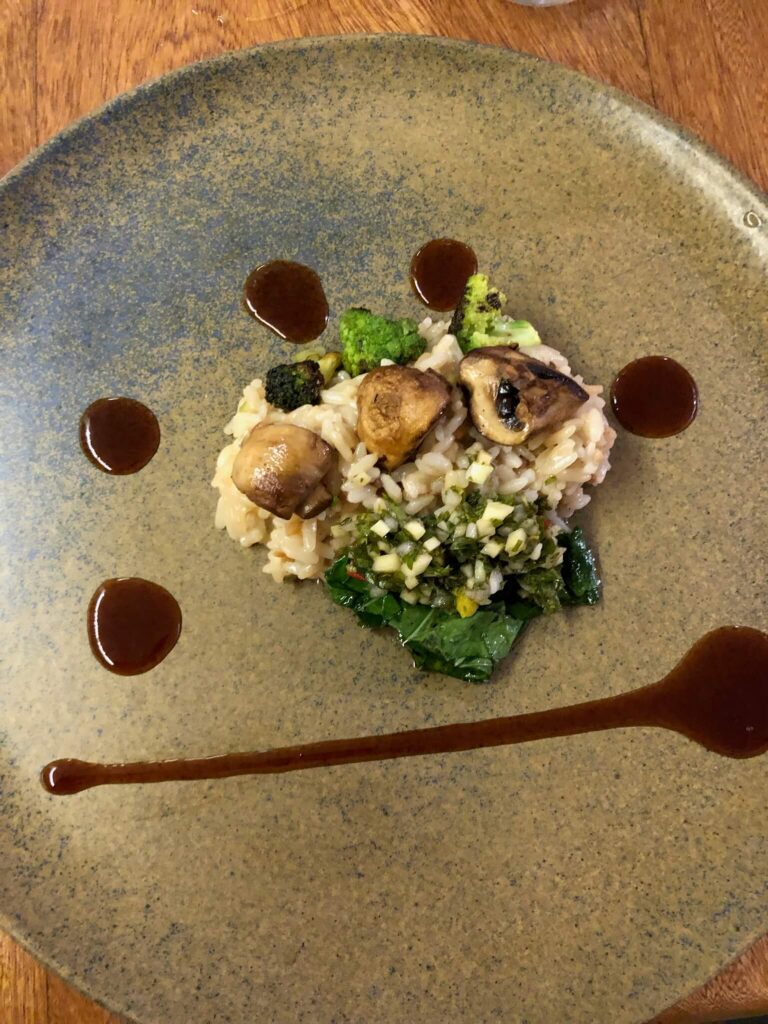 Op een bord ligt een maaltijd culinair opgediend: een kleine ortie rijst met daarbovenop 3 champignons en een sausje ernaast