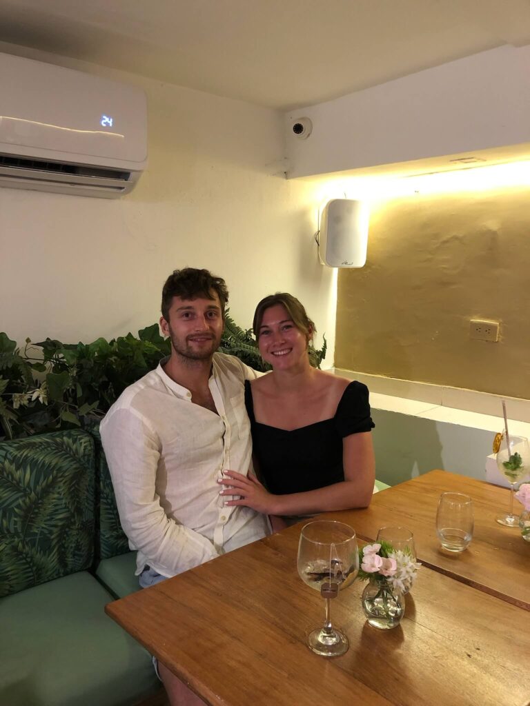 Niels en ik zitten aan tafel en poseren lachend voor de camera. Op de tafel staan een paar lege glazen