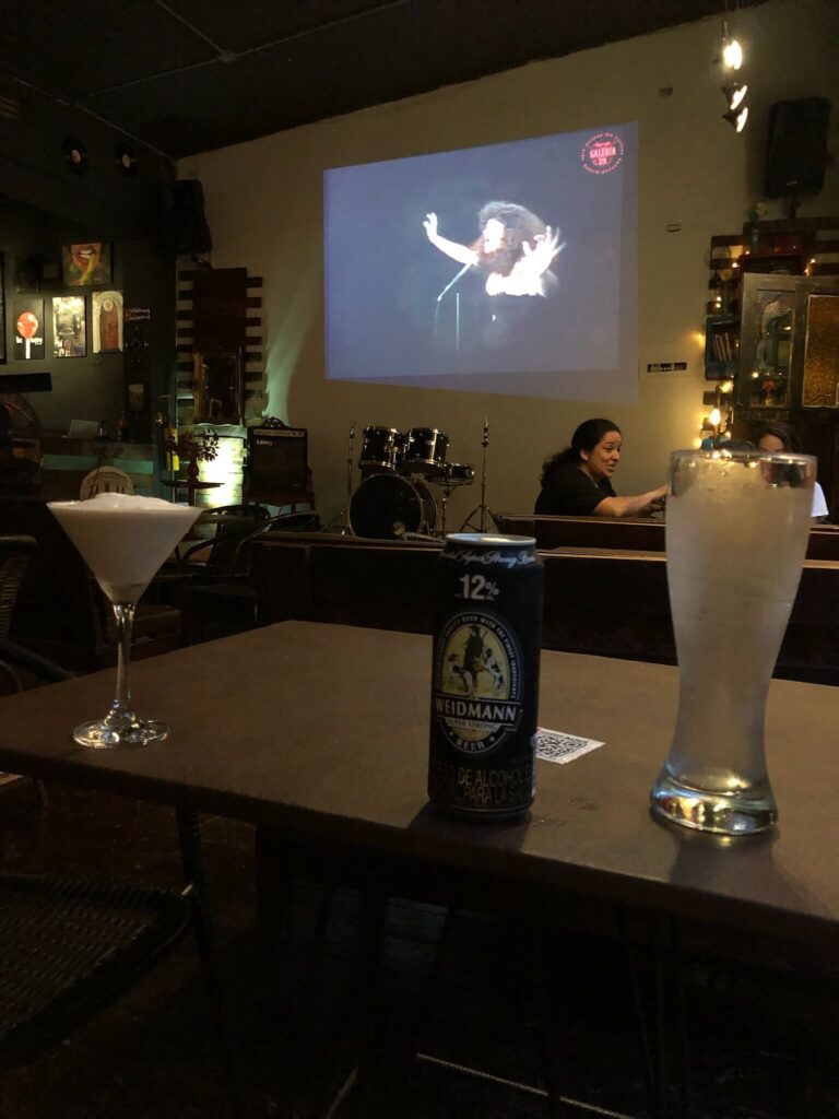 Een lage zittafel met een cocktail en een biertje met in de achtergrond op de muur een filmbeeld van een band