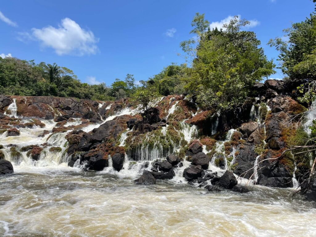 Een foto van alle rotsen die in de rivier liggen waar het water zich doorheen wringt waardoor er allemaal kleine watervallen te zien zijn die over de rotsen heen lopen