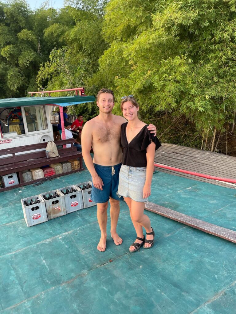 Niels en ik staan poserend op de boot, te lachen in de camera. Achter ons zie je bomen en de rest van de boot