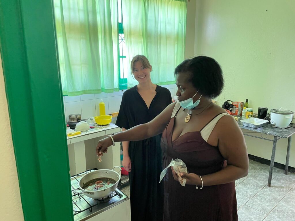 Sandra en ik staan in de keuken. Sandra doet wat kruiden in de pan. Ik sta achter haar en kijk lachend in de camera