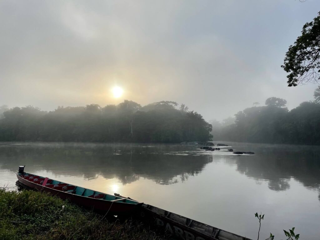 Je ziet de rivier met op de achtergrond de laag hangende zon. Je ziet ook bomen aan de andere kant van de rivier staan. Het is een beetje een mystieke foto