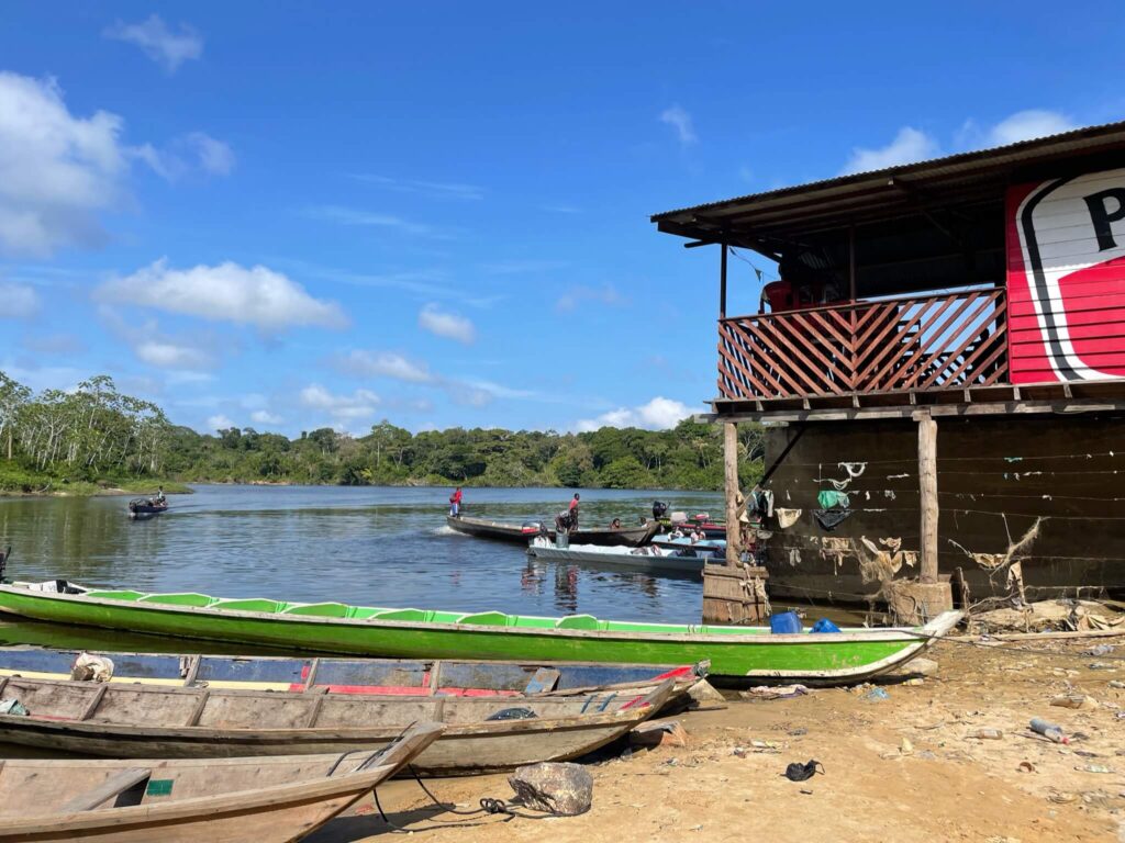 Er liggen 3 houten lange smalle boten naast elkaar op de kade en deels in de rivier. Deze kun je pakken om de rivier af te varen.