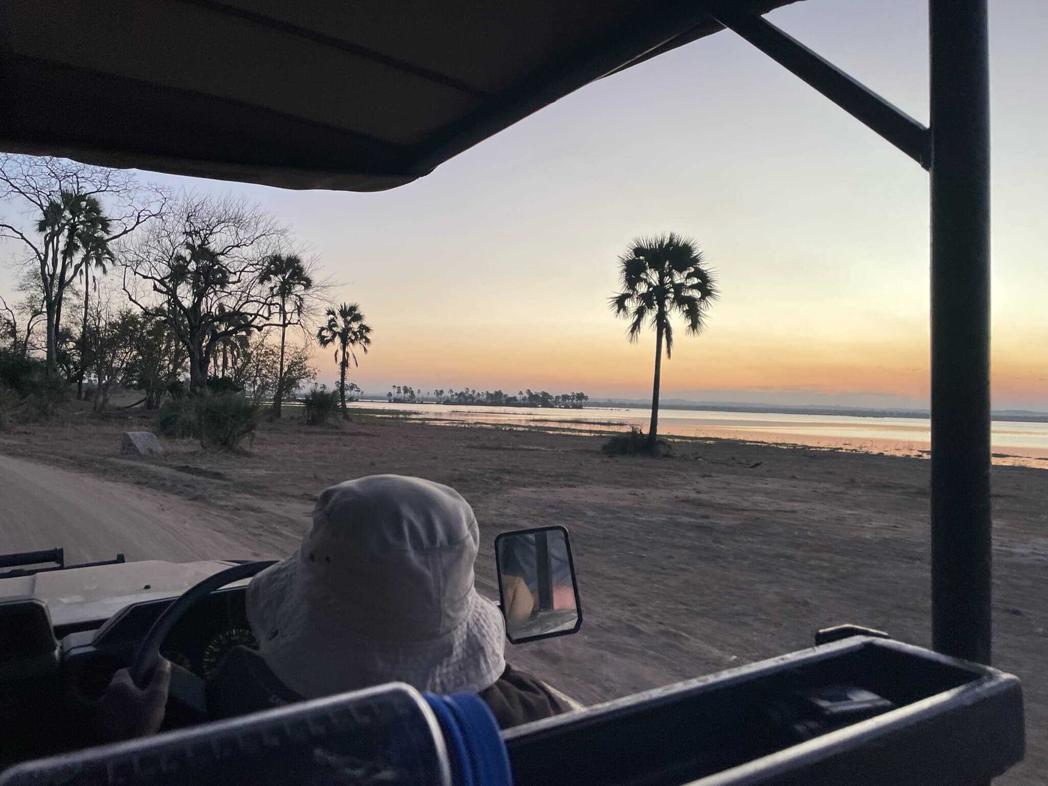 Foto genomen vanuit de jeep met uitzicht op het water, de palmbomen, en zonsondergang