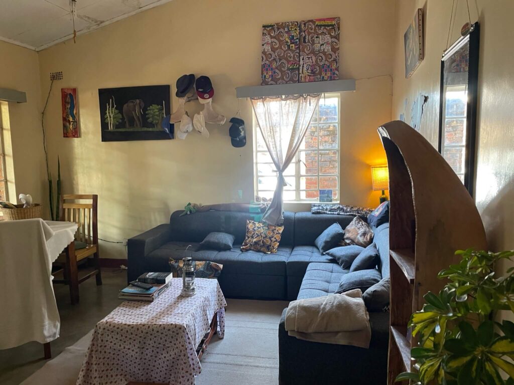 De woonkamer in ons verblijf in Zomba: je ziet een grijze hoekbank en een salontafel met daarnaast nog een houten eettafel