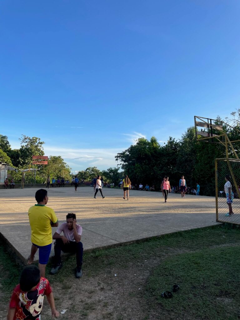 een voetbaldveld met een paar lokale mensen die aan het voetballen zijn met daarachter groene bomen