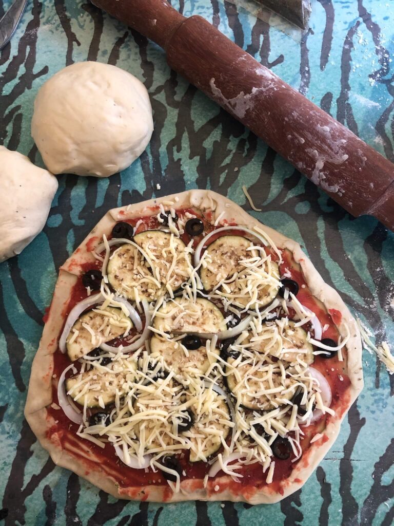 Onze zelfgemaakte pizza. Je ziet het deeg op de tafel leggen. De pizza is belegd met tomatensaus, courgette, ui en kaas