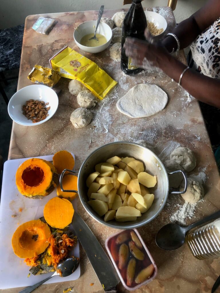 Een tafel vol met ingrediënten om roti te maken: je ziet pompoen, aardappel en roti-deeg
