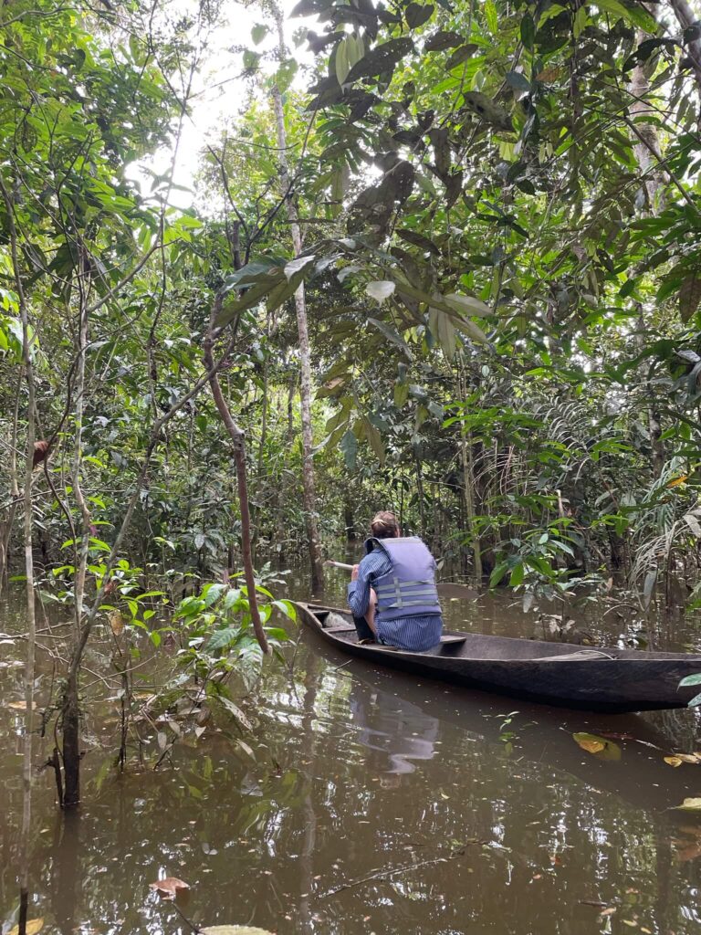ik zit in een bootje dat over de rivieren van de amazone vaart met allemaal groene bebossing om me heen