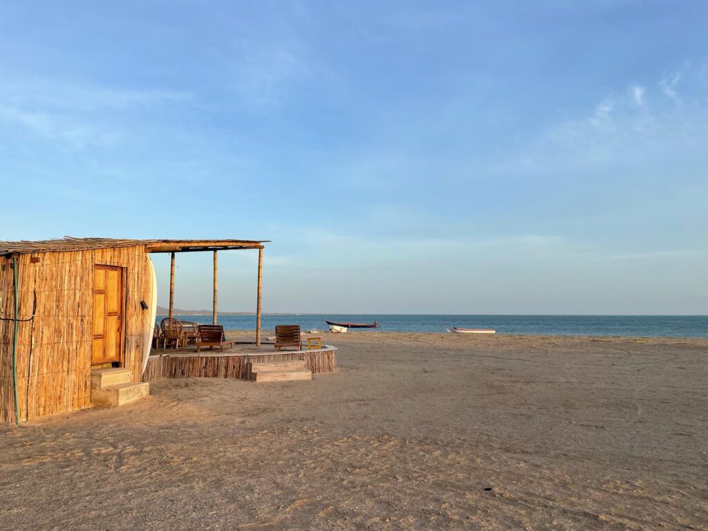 Een rieten huisje op het strand met daarachter de zee en een strakblauwe lucht