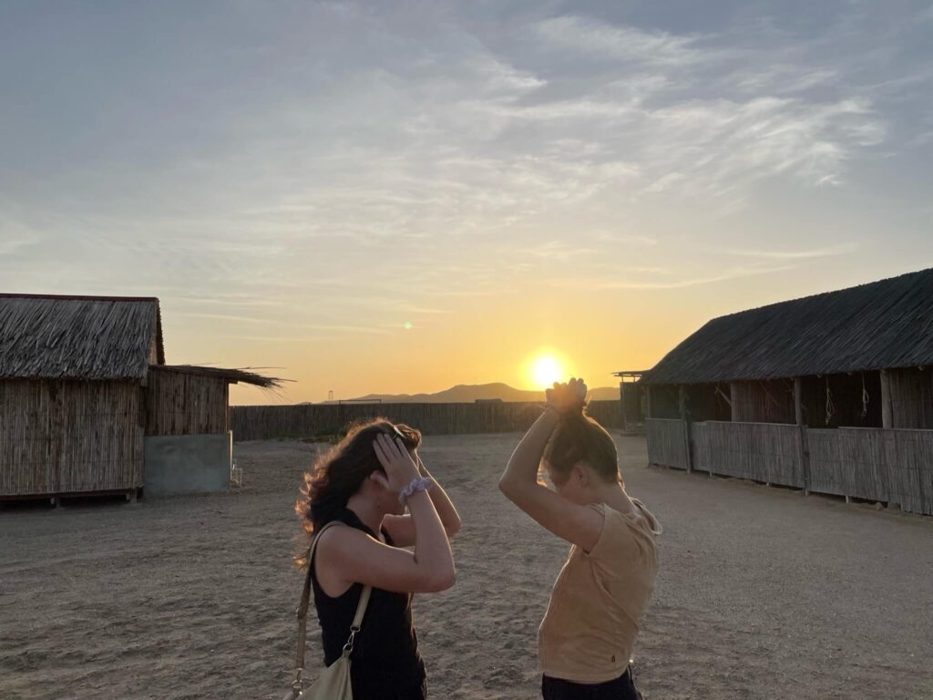 Synia en ik staan tegenover elkaar, beiden ons haar vast te houden omdat de wind het in de war waait. Op de achtergrond zie je de zon ondergaan