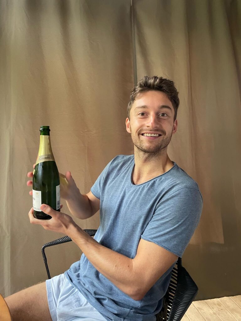 Niels houdt een fles prosecco omhoog en lacht in de camera