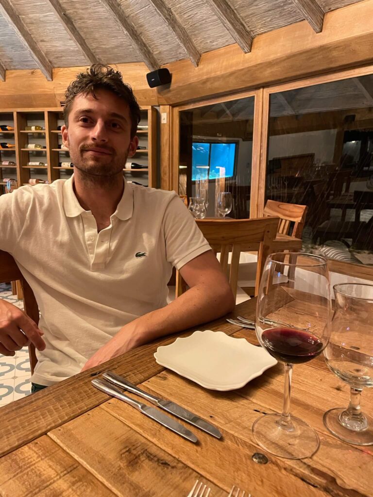 Niels zit in het restaurant. Hij zit aan tafel met een glas rode wijn en een leeg bord naast hem