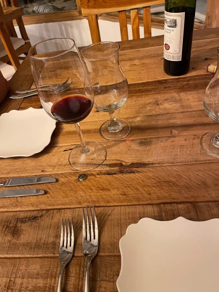 Houten tafel met daarop een wijnglas met rode wijn. Verder zie je bestek en 2 borden liggen