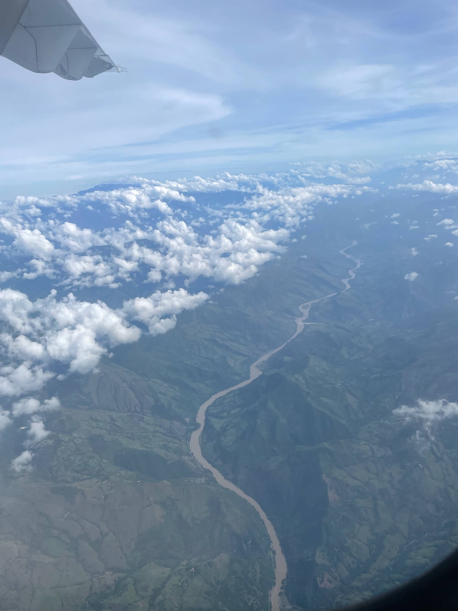 Deze foto is genomen vanuit het vliegtuig. We kijken hier vanuit het raam neer op een geweldig mooie bergketen waar een smalle rivier doorheen loopt