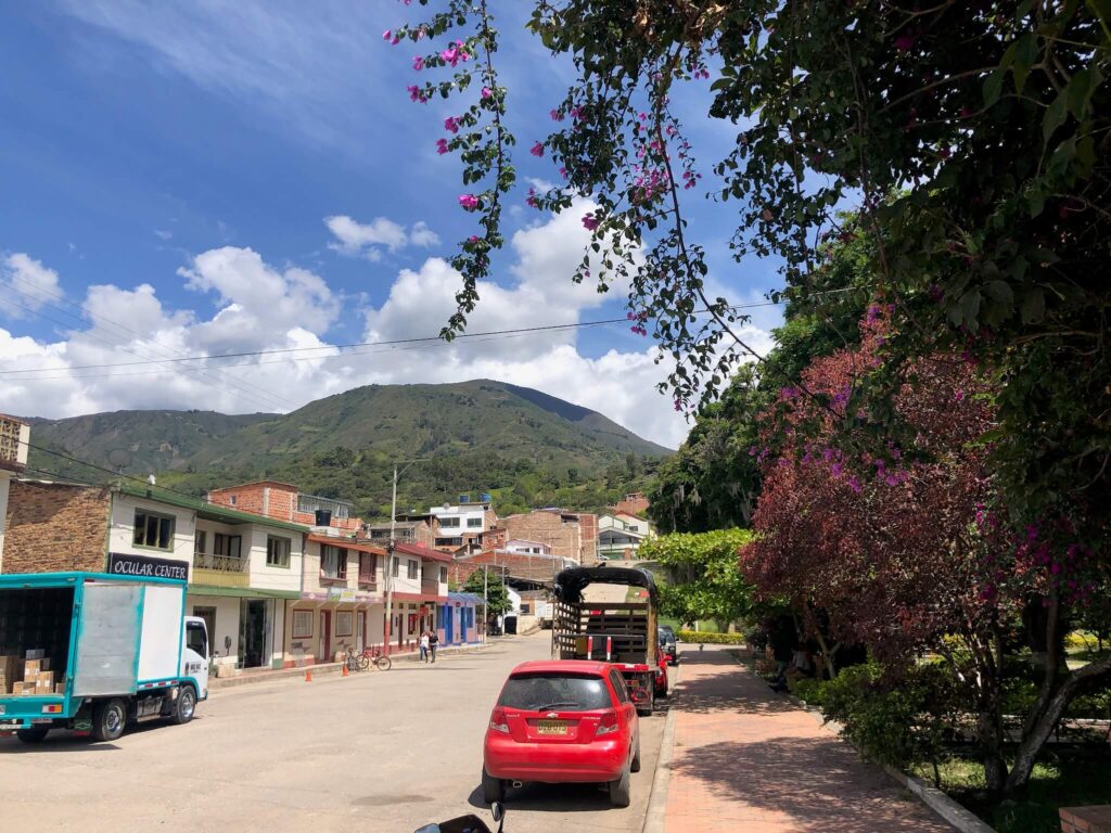 een brede straat in soatá met links wat huisjes, rechts een rode auto en in de verte een hoge groene berg