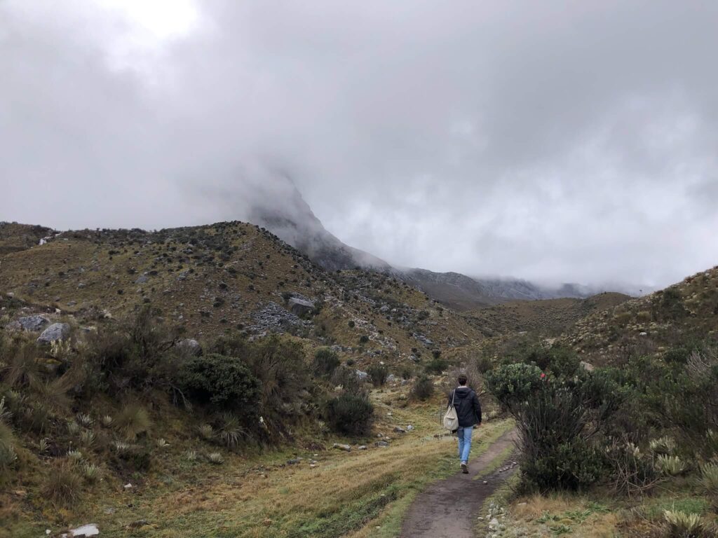 Niels loopt op een bergpad met grijze wolken boven hem en groene bergen links en rechts van hem