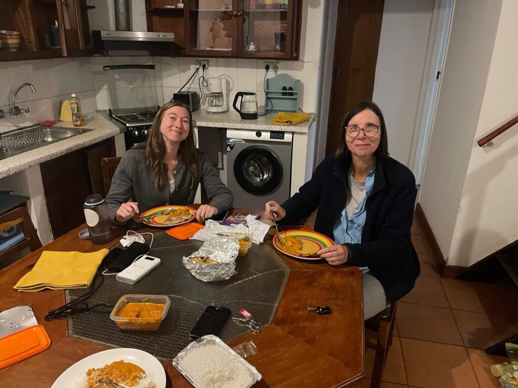 Ik zit samen met m'n moeder aan een eettafel. We lachen naar de camera. Op de tafel staat Indiaas eten
