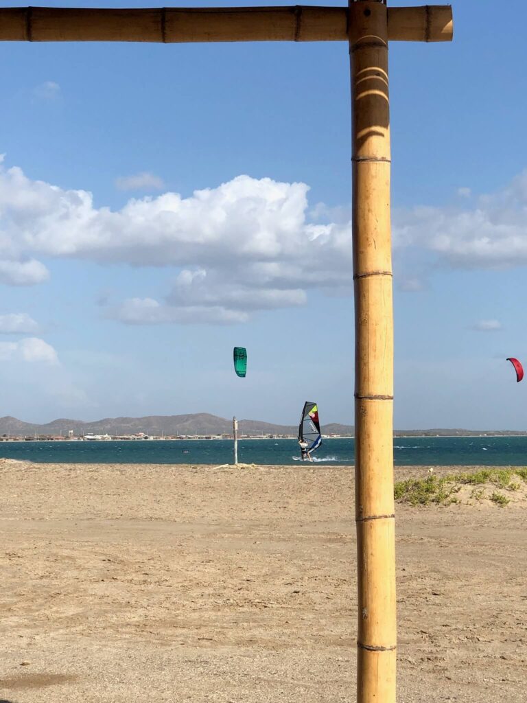 Niels is aan het windsurfen op de zee en voor de zee kun je het strand zien liggen