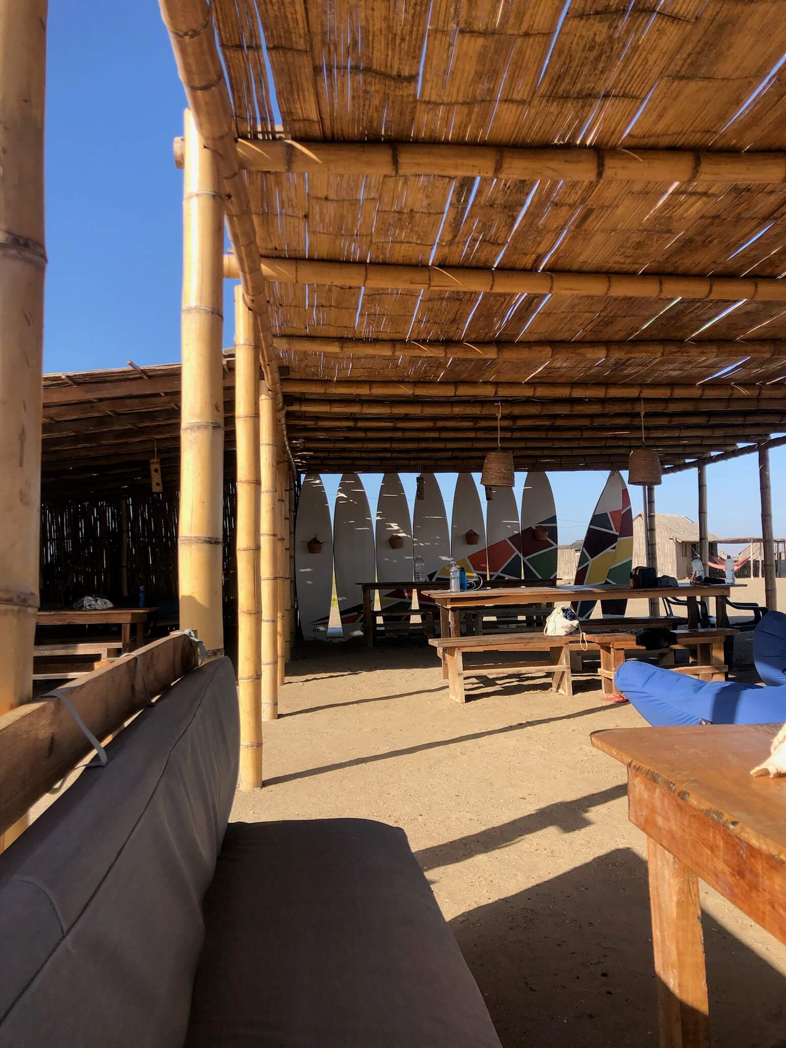 De woonkamer van het hostel met verschillende surfplanken naast elkaar op rij, onder een rieten dak