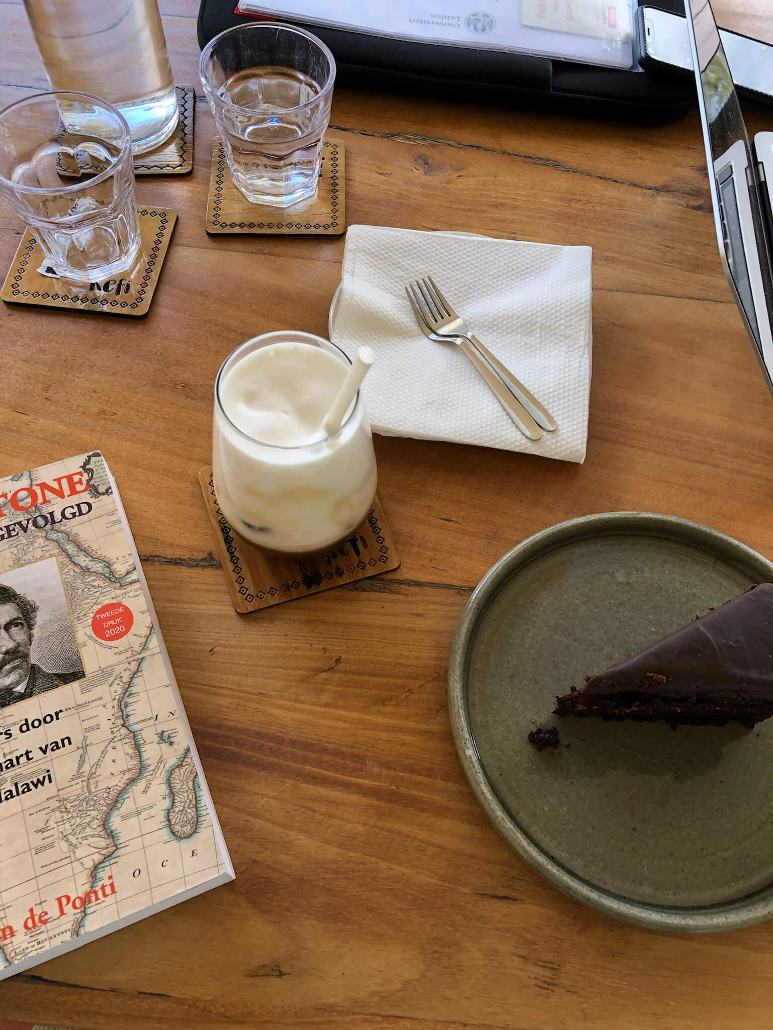 Foto van een tafel met daarop een bord met een stukje chocoladetaart en daarnaast een boek en een koffietje