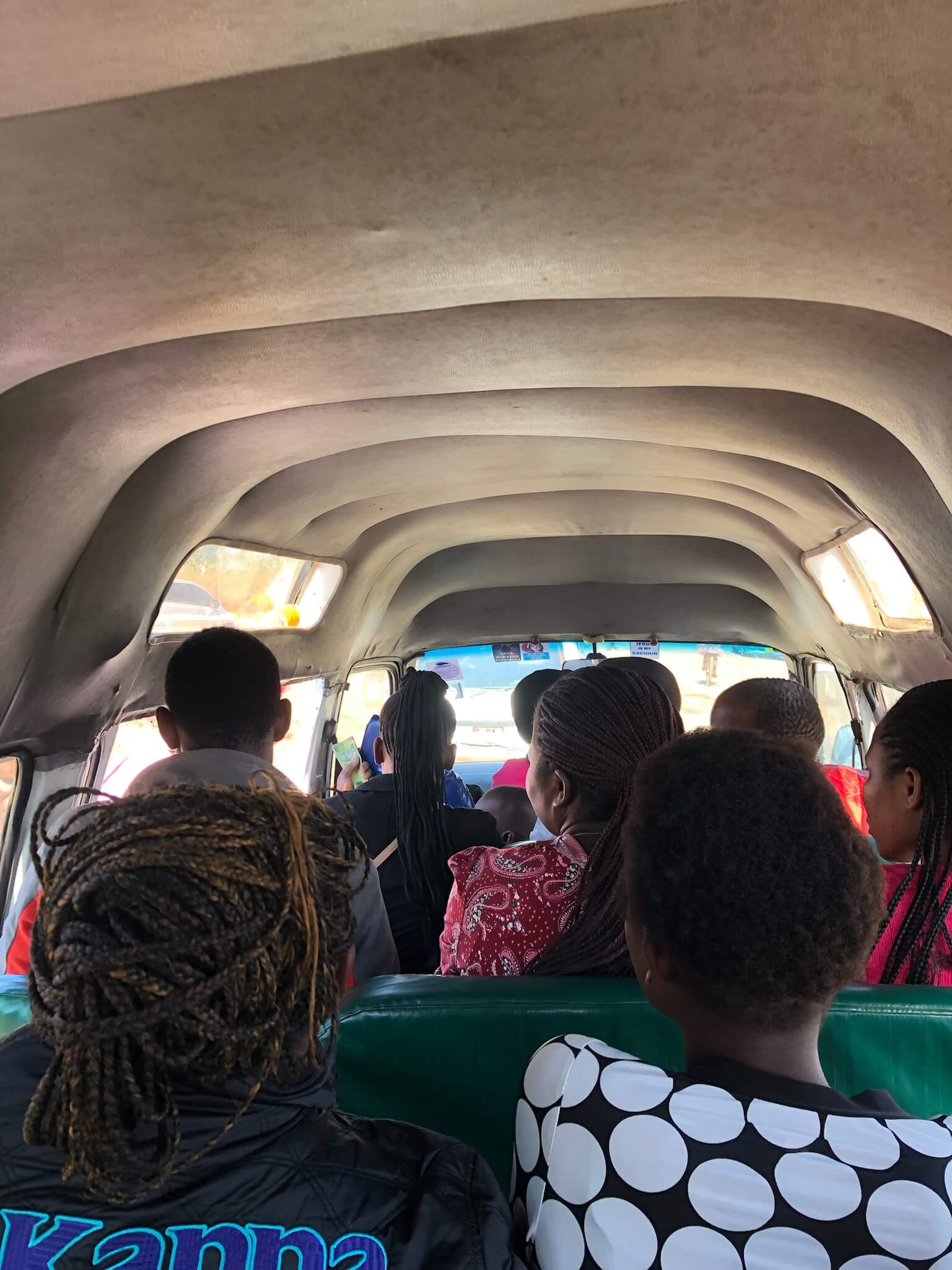 Een foto van de binnenkant van de mini-bus. Er zitten een aantal lokale mensen voor mij in de bus. Ze zijn gefotografeerd vanaf de achterkant