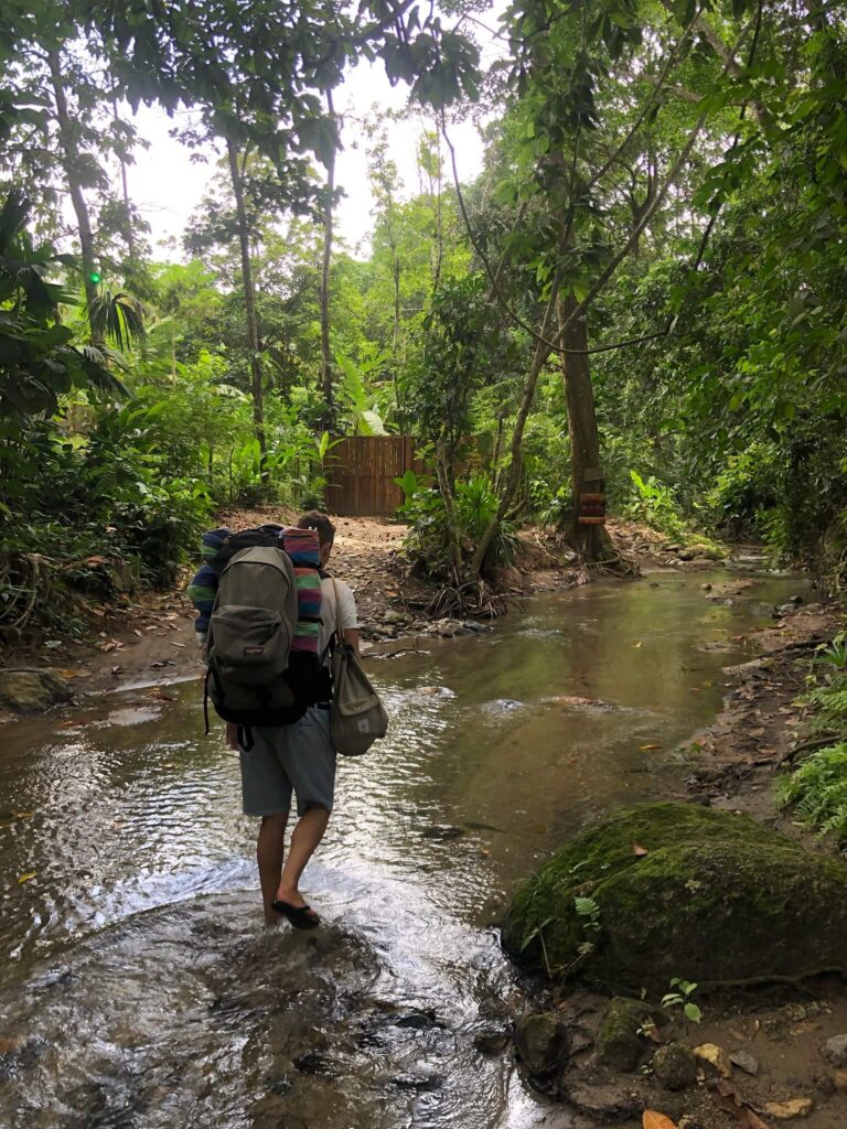 Niels loopt door een rivier door de jungle met een backpack op z'n rug