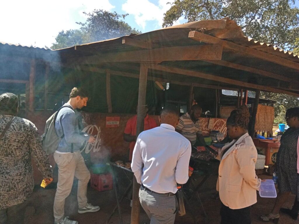 Niels bestelt lunch bij een lokaal lunchtentje. Er ligt kip op de grill. Naast hem staan allemaal mensen