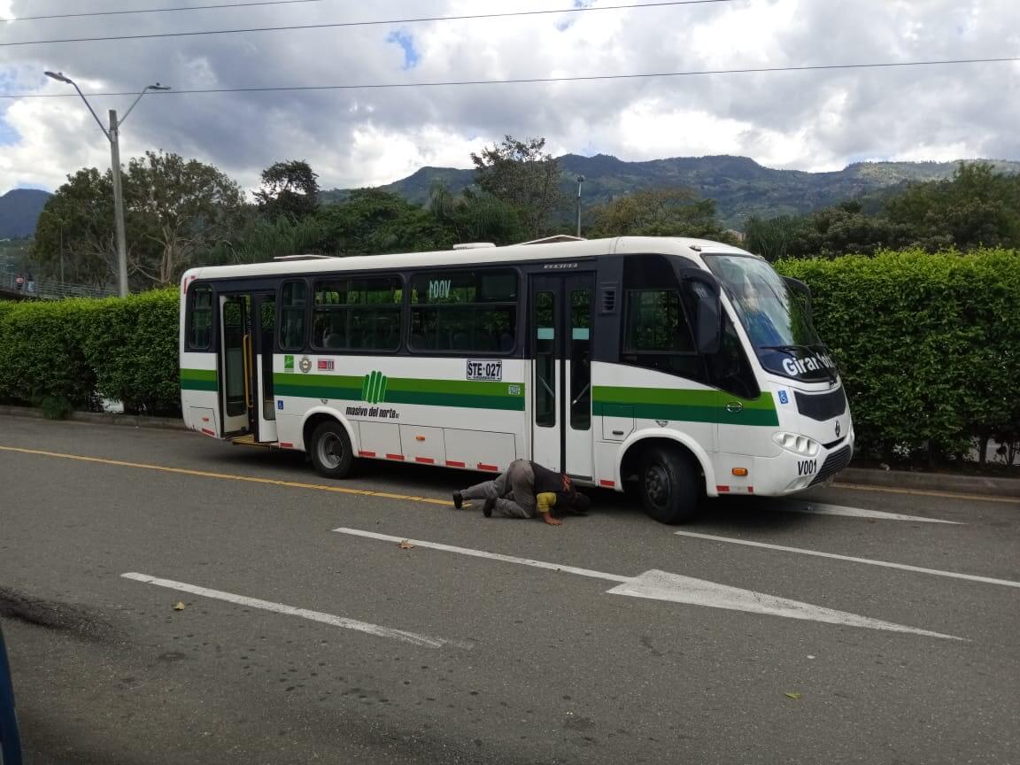 De kapotte bus: wit met een groene streep. Op de straat liggen 2 mannen onder de bus te kijken wat er aan de hand is