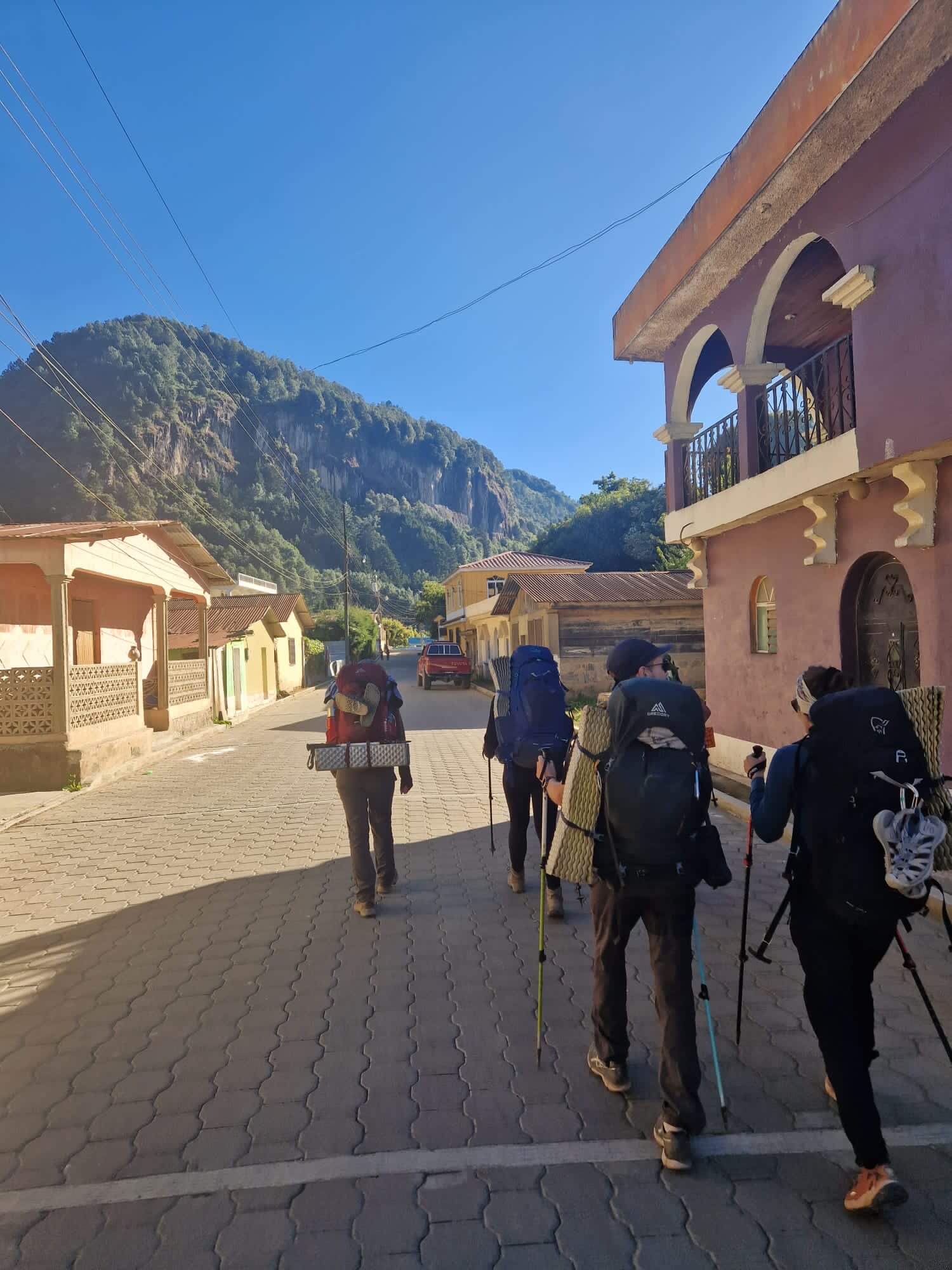 Een aantal mede-wandelaars lopen voor me uit. Ze zijn allemaal bepakt met zware backpacks. In de verte zie je een groene berg.