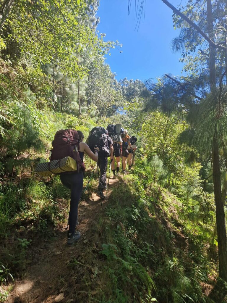 Mede-hikers lopen voor me uit op een smal wandelpad dwars door het groen heen. Iedereen is bepakt met zware backpacks