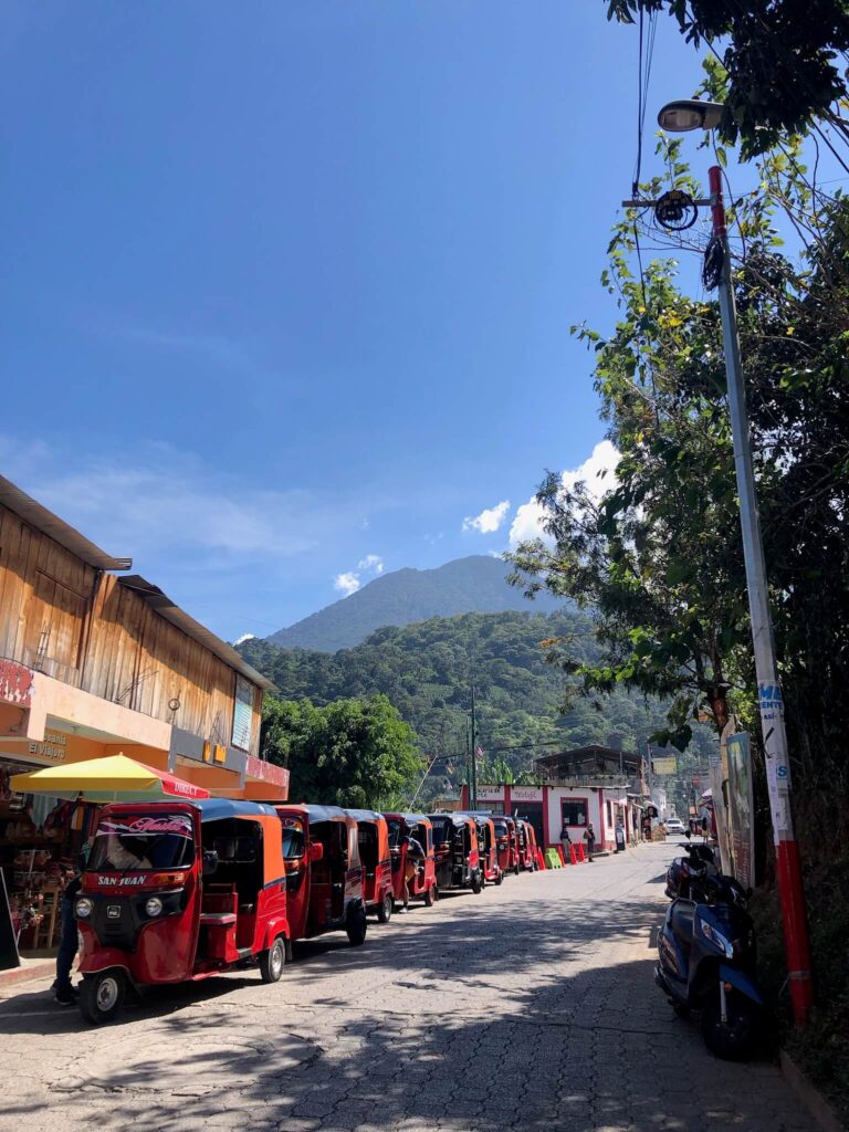 Een andere rustige straat in San Juan. De rode tuctucs staan achter elkaar links van de straat opgesteld. In de verte zie je een berg