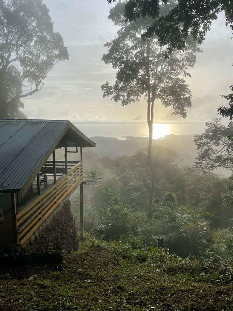 Een prachtig mooi uitzicht vanaf de berg, kijkend op het water in de verte. De zon zakt in het water. Er is verder veel hoogteverschil en je ziet de jungle tussen het water en de fotograaf
