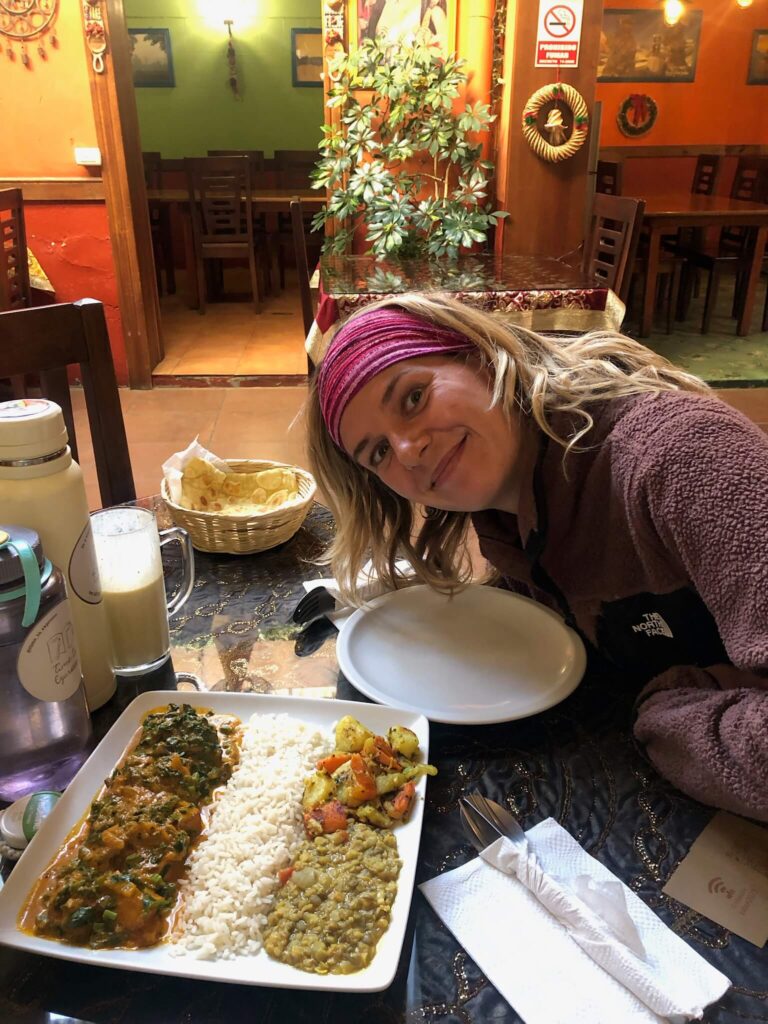 Een foto van Yaar die lacht naar de camera. Voor haar op tafel staat een bord met heerlijk Indiaas eten