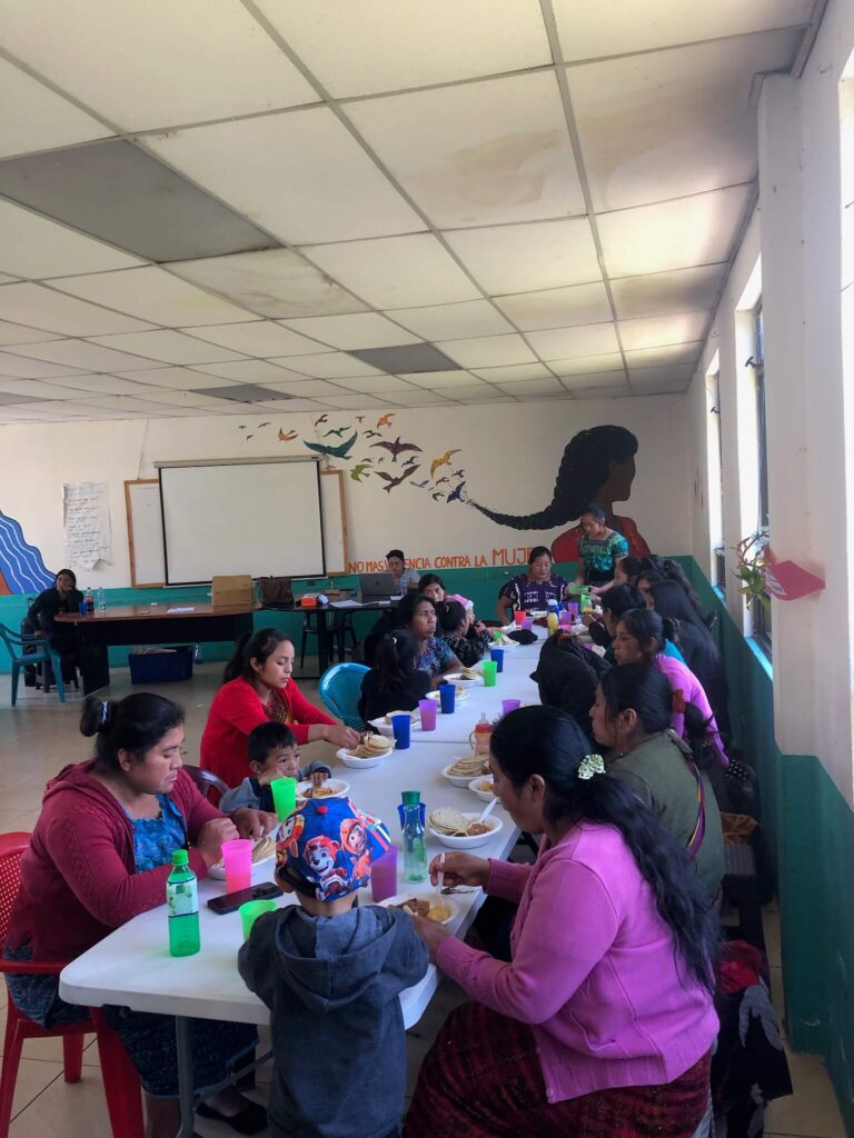Een lang gedekte tafel met allemaal vrouwen die hieraan zitten te eten