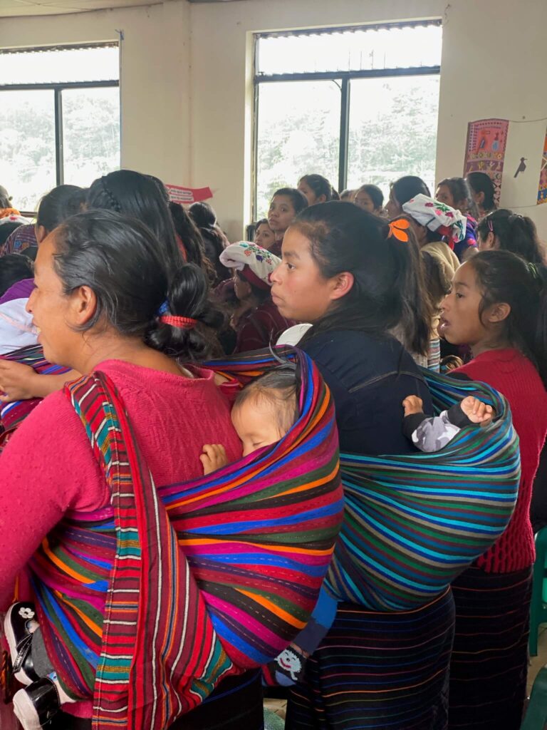 Er staan een paar vrouwen op de foto die aanwezig zijn bij de grote bijeenkomst. Ze hebben doeken om hun rug waar ze hun baby's in dragen