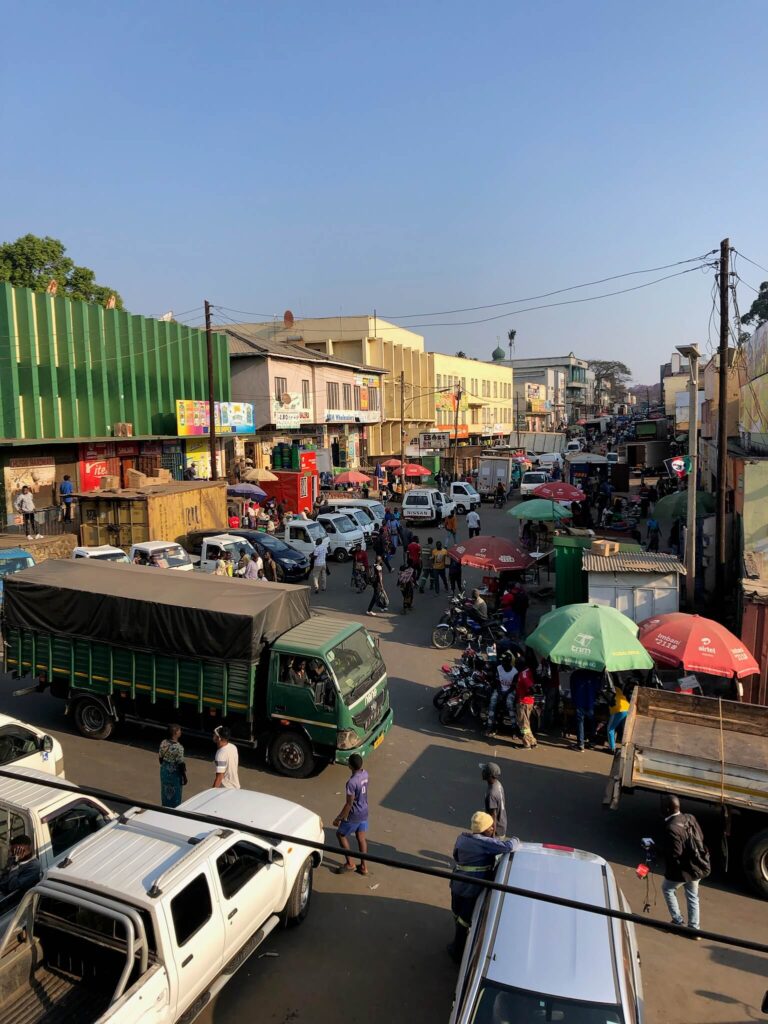 Je ziet een drukke straat met allemaal vrachtwagens en auto's en parassollen waar mensen onder zitten
