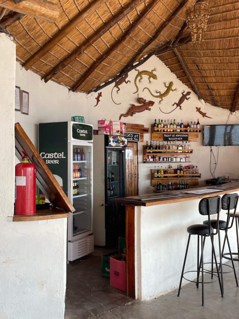 De bar bij het verblijf: een witte muur met houten bar en rieten dak. Er staan barkrukken aan de bar