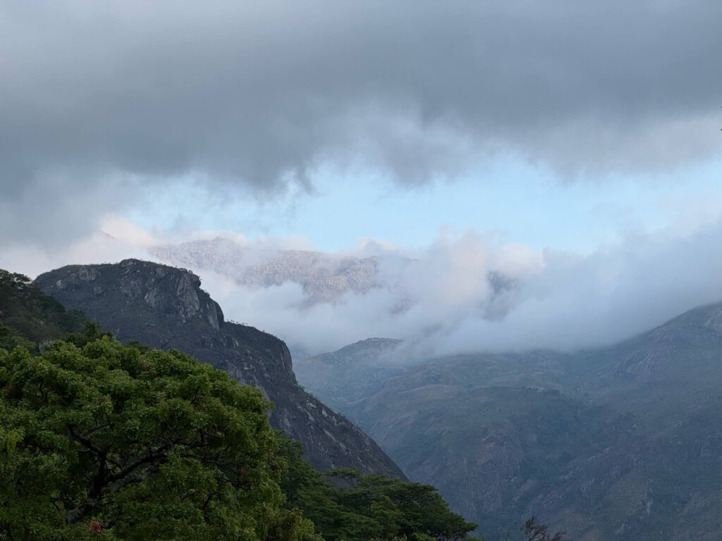 Je ziet 2 bergen op de heuvel met daarboven wolken en achter de wolken zie je een topje van een verre berg uitsteken