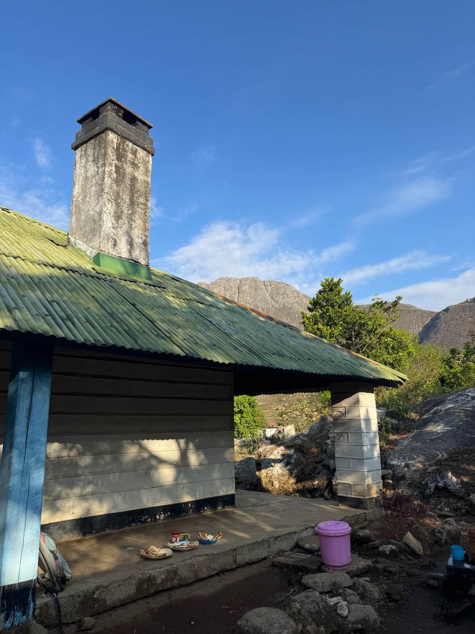 Het huisje waar wij deze nacht in hebben geslapen met op de achtergrond een berg. Op de veranda van het huisje staan 3 eetbordjes met ons ontbijt