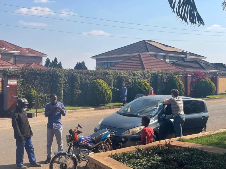 Je ziet een foto van een straat in Lilongwe. De taxi is net aan komen rijden, voor hem staat de motor die hij moest volgen