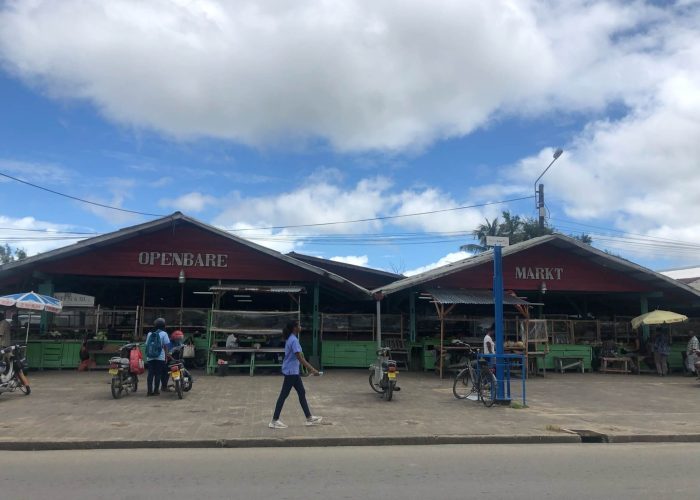 De markt in Nickerie van de buitenkant gefotografeerd. Je ziet eigenlijk gewoon een groot huis met dak. Daarbinnen bevinden zich allemaal kraampjes