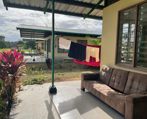 De voorkant van ons huis: de veranda! Hierop staat een bank en verderop zie je een waslijn met kleding hangen