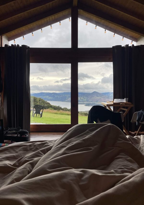 uitzicht dat we hebben vanuit het bed in het huisje op een mooi meer met een groen grasveld en bergen erachter